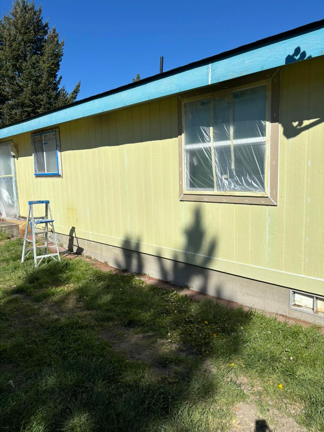 A yellow house with a blue roof is being painted.