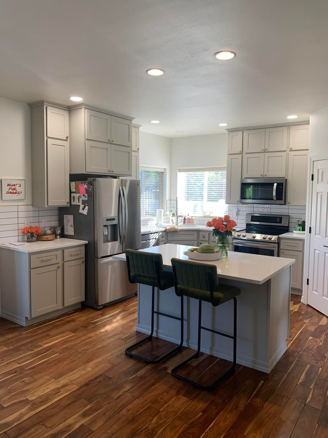 A kitchen with white cabinets , stainless steel appliances , hardwood floors and a large island.