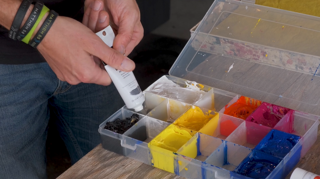 man putting acrylic paint in a paintbox