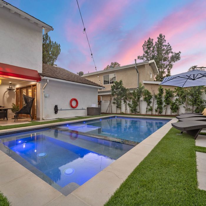 Backyard pool with spa, lawn, and patio at dusk; pink and blue sky.