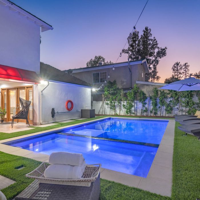 Backyard pool at dusk with a house, grass, and lounge chair.