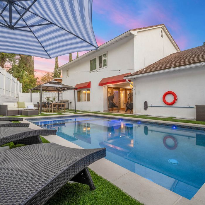 Backyard with a pool, lounge chairs, and a two-story white house with red awnings.