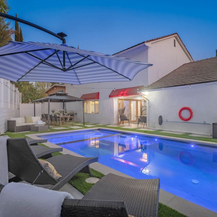 Backyard pool with lounge chairs, umbrella, and illuminated water at dusk.