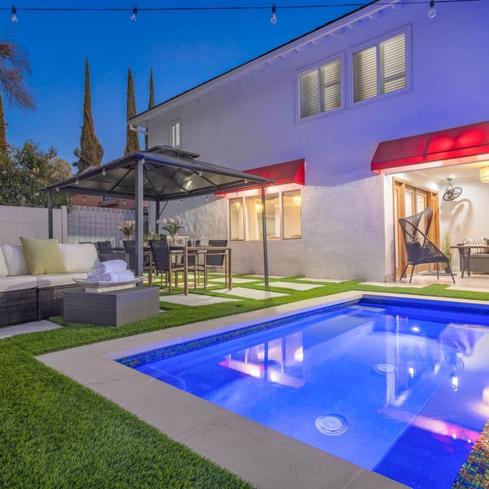 Backyard pool area with outdoor seating, dining, and string lights, set against a two-story white house.