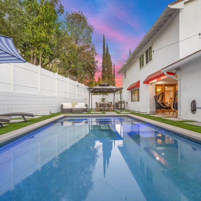 Backyard pool with white house, lounge seating, and dining area at sunset.