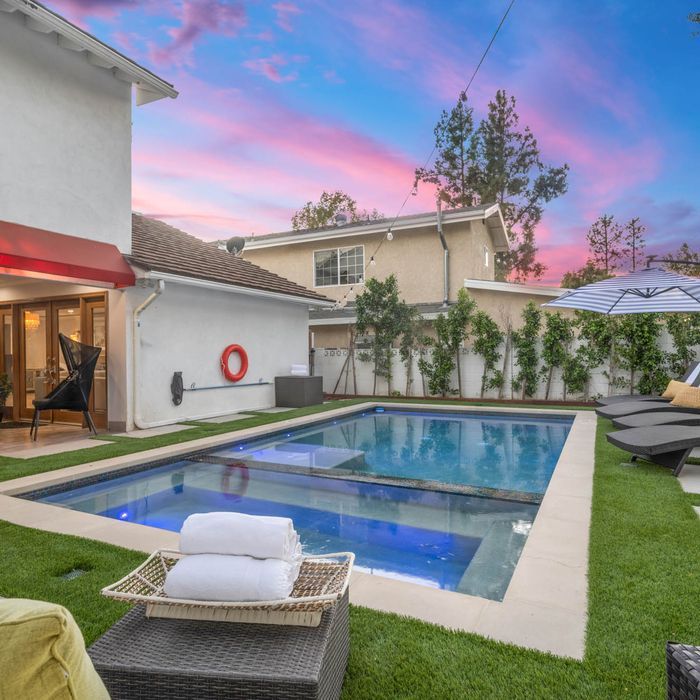 Pool and backyard at sunset with lounge chairs and towels.