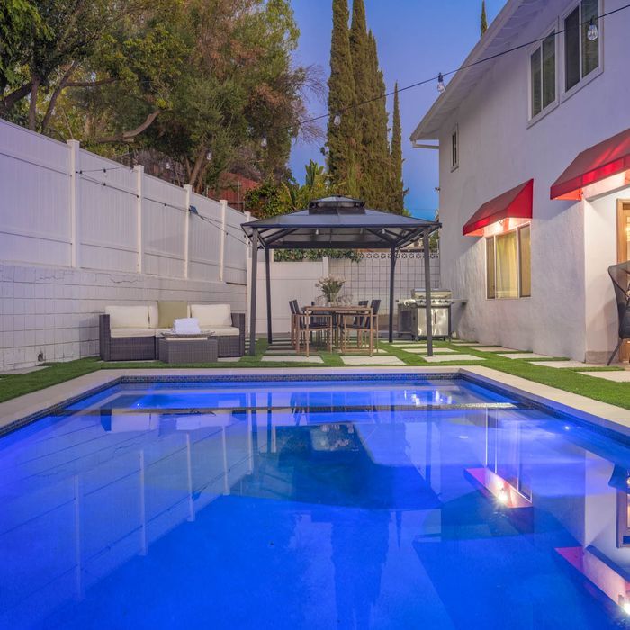Backyard pool with a gazebo, outdoor furniture, and a white house with red awnings.