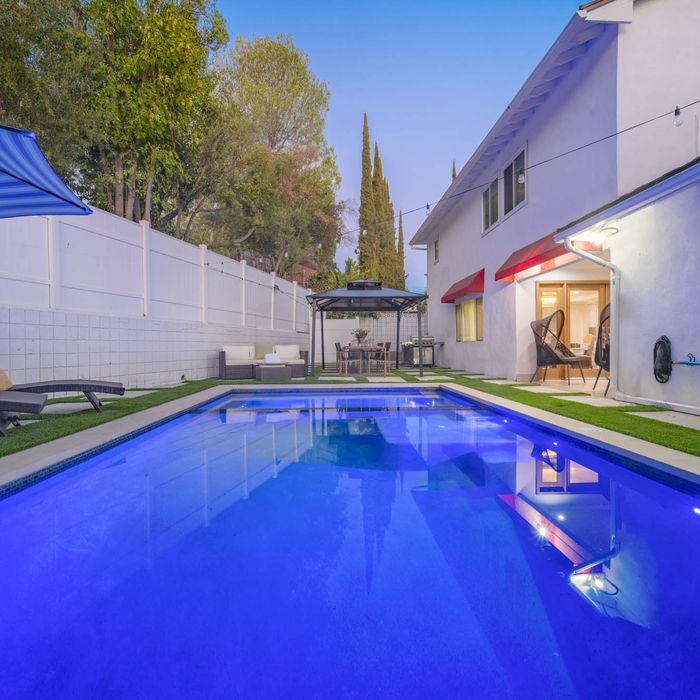Backyard with a pool, seating areas, a pergola, and a two-story house. Blue sky overhead.
