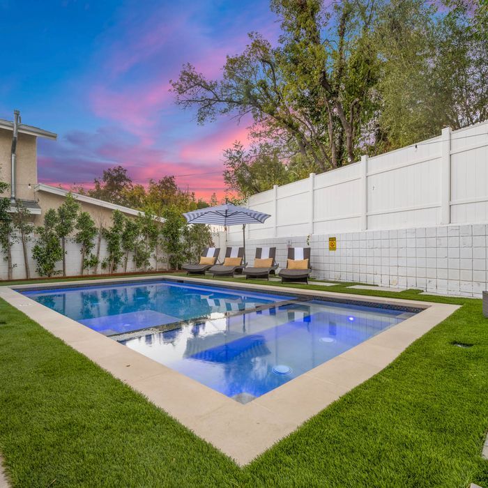 Backyard pool with lounge chairs, umbrella, and a colorful sunset.