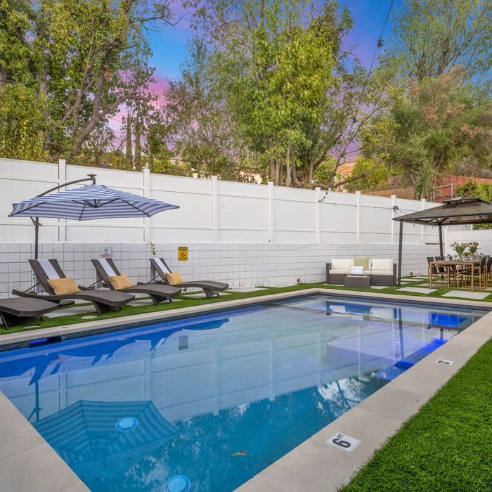 A backyard pool with lounge chairs, a gazebo, and a striped umbrella.