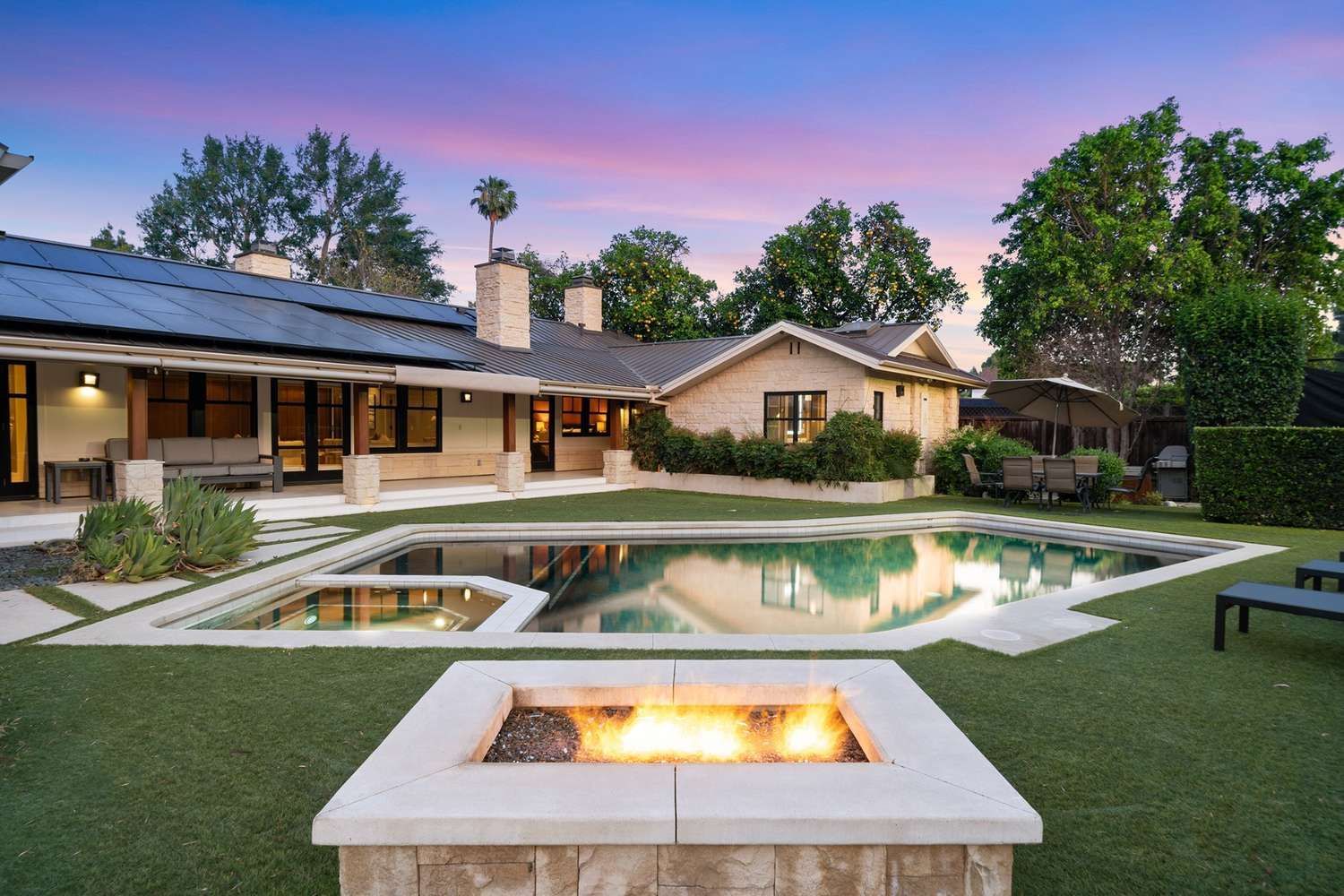Backyard with pool, fire pit, green lawn, and house at dusk.