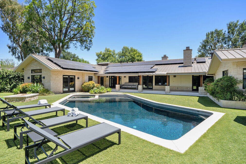 Backyard with pool, house, lounge chairs, and green grass on a sunny day.
