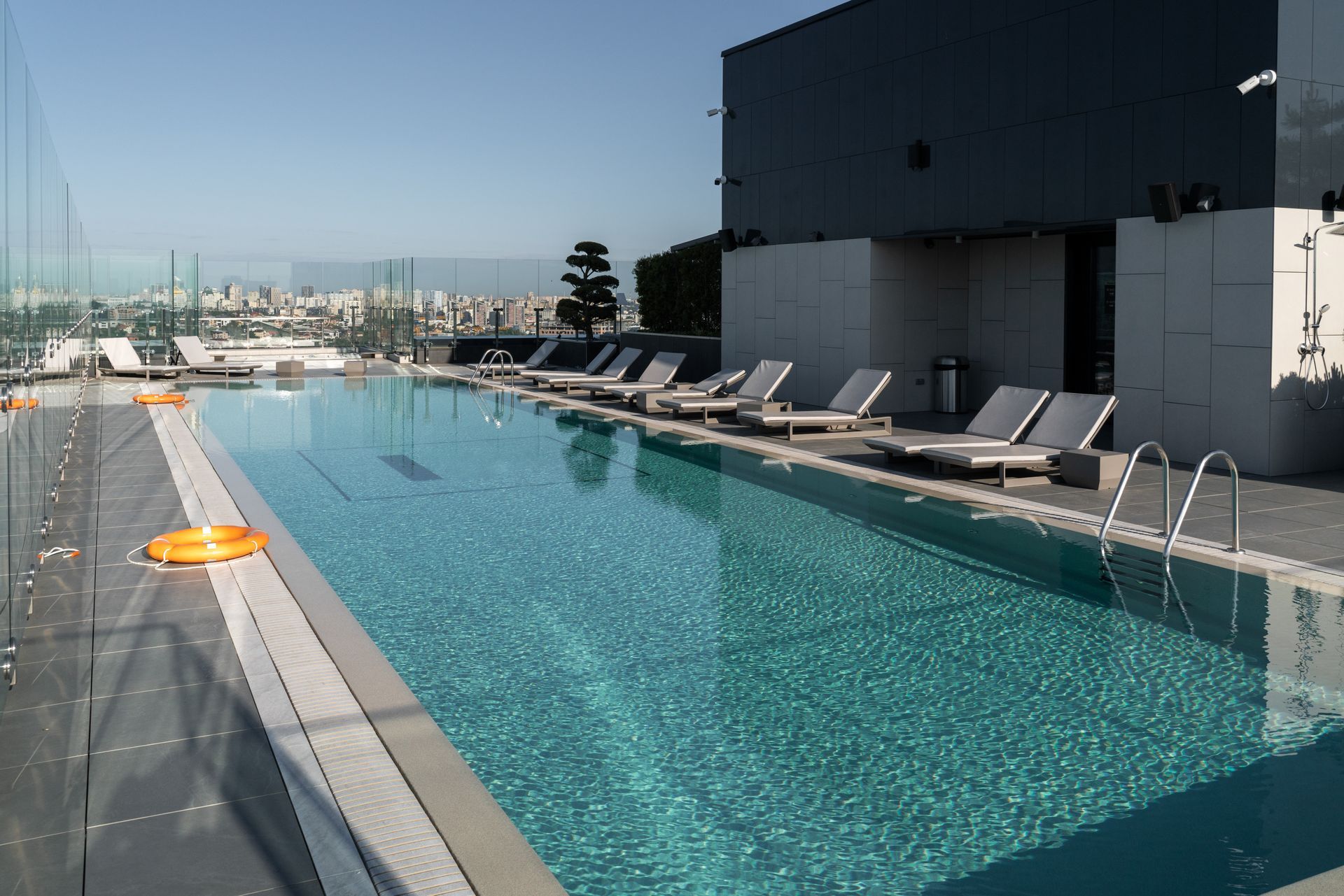 Rooftop pool with chaise lounges, life preservers, and a city view on a sunny day.