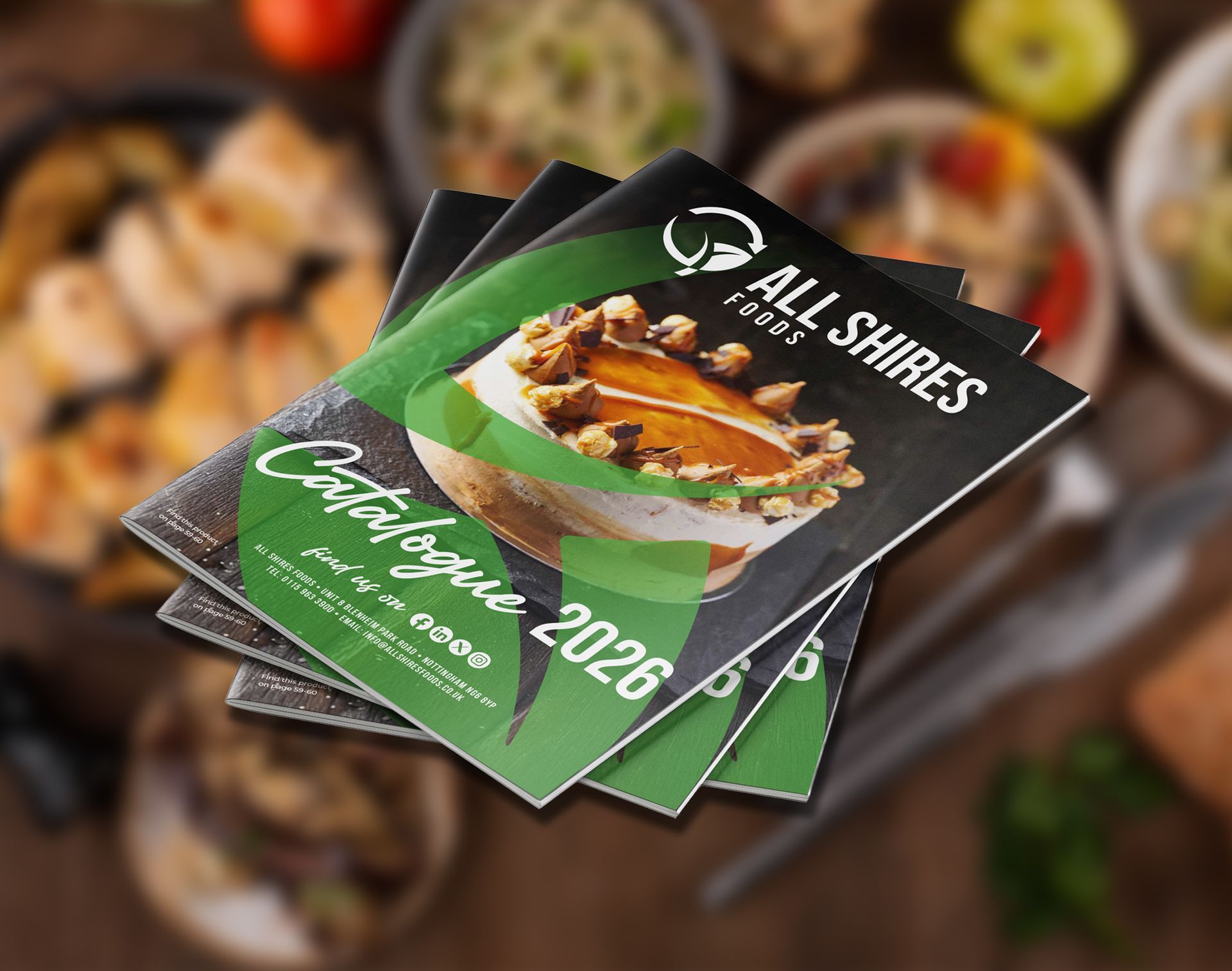 A stack of All Shires Food 2026 catalogues featuring a dessert graphic, set against a blurry kitchen background.