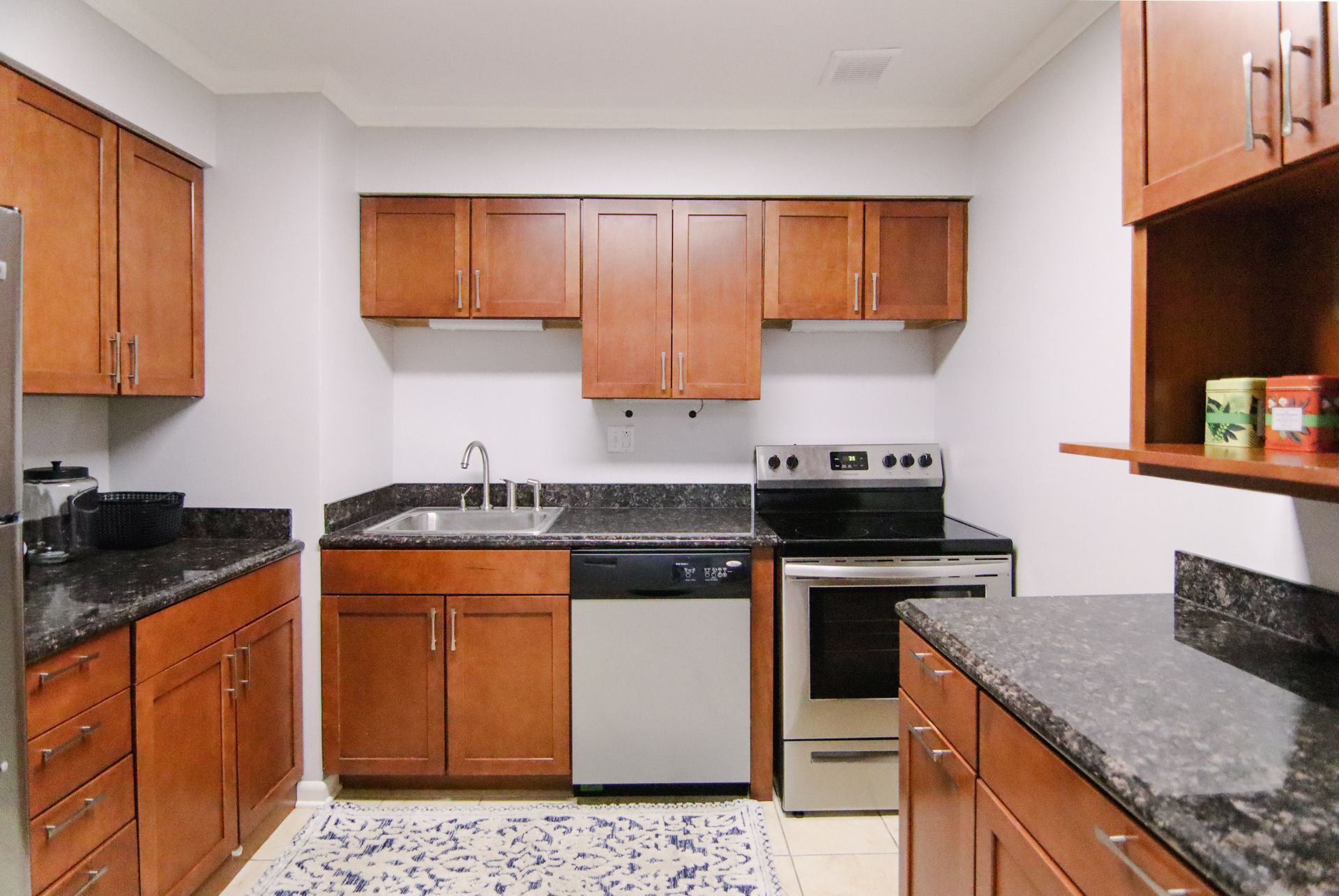Small kitchen with brown cabinets, stainless steel appliances, and dark countertops.