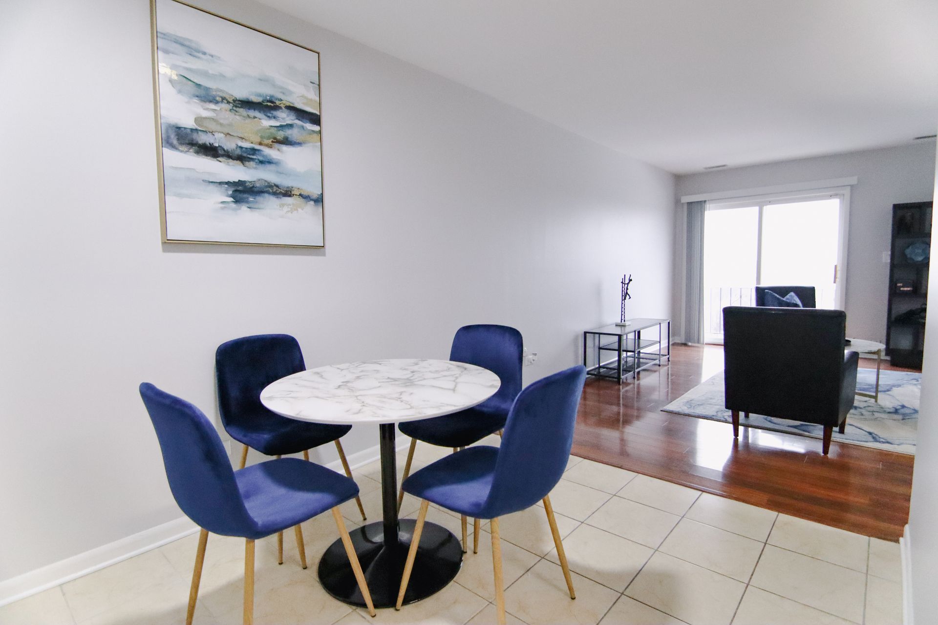 Dining area with marble table and blue chairs, leading to living room with sofa and balcony door.