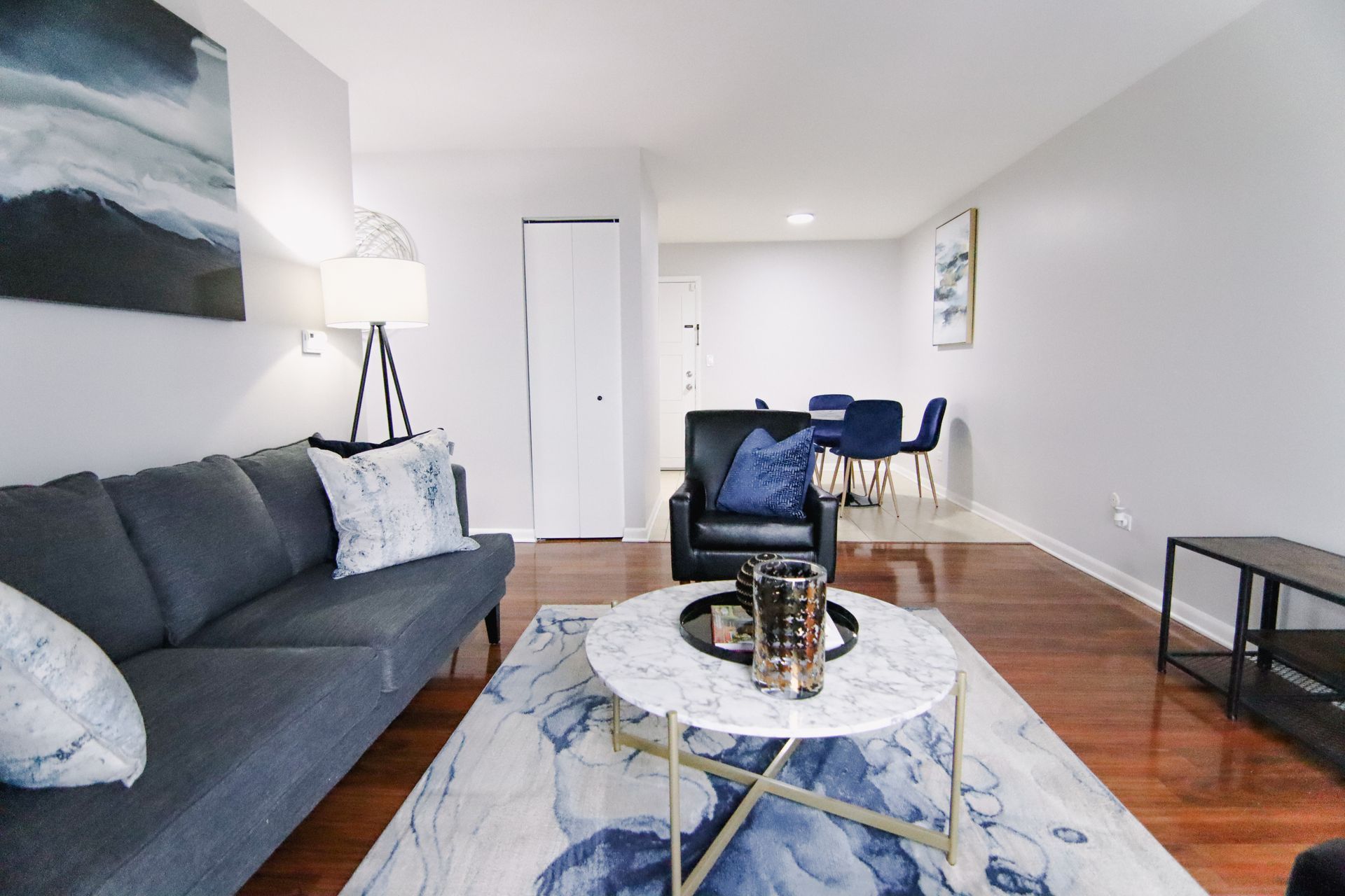 Living room with blue sofa, marble coffee table, and dining area in the background.