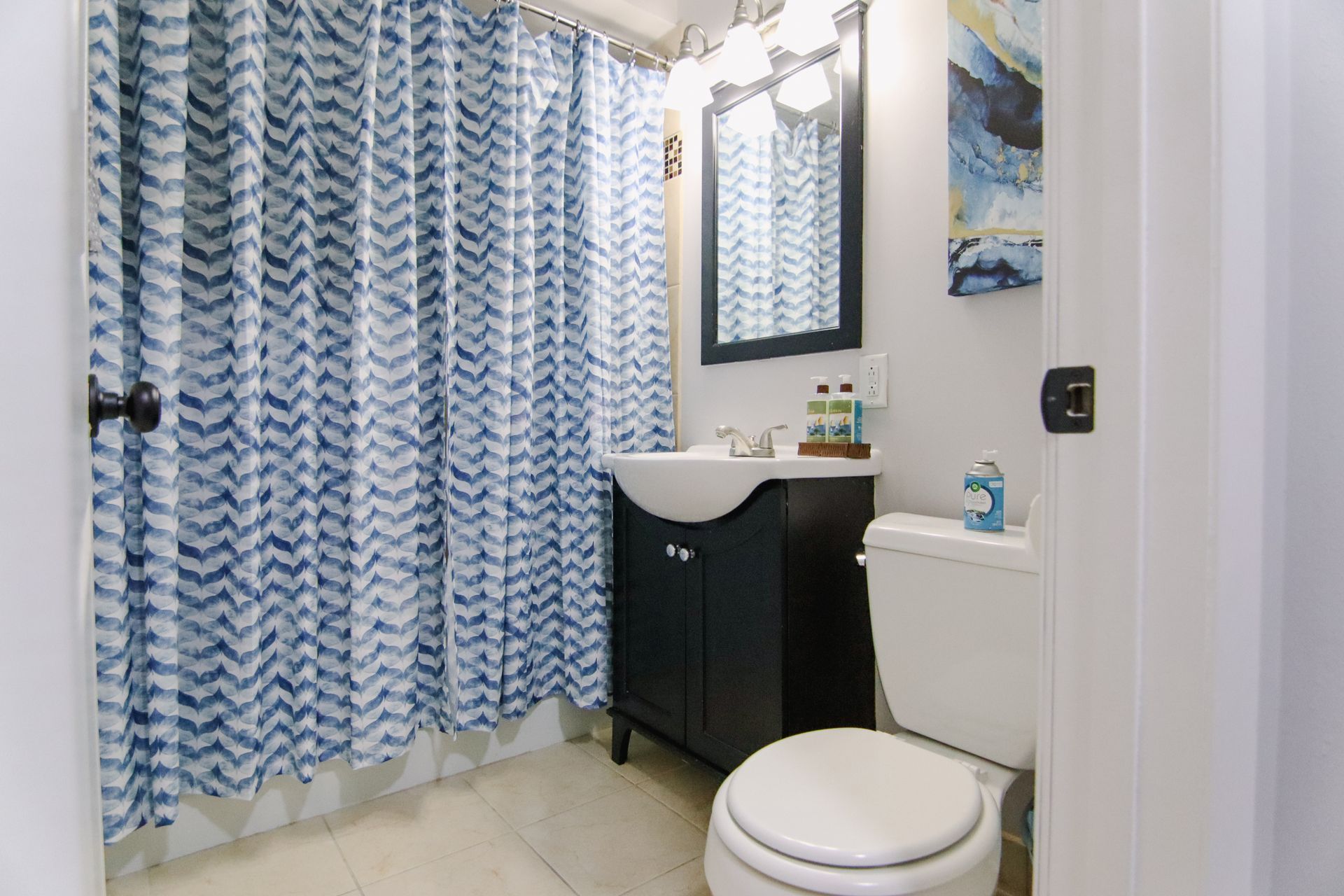 Bathroom with blue chevron shower curtain, dark vanity, white toilet and walls.