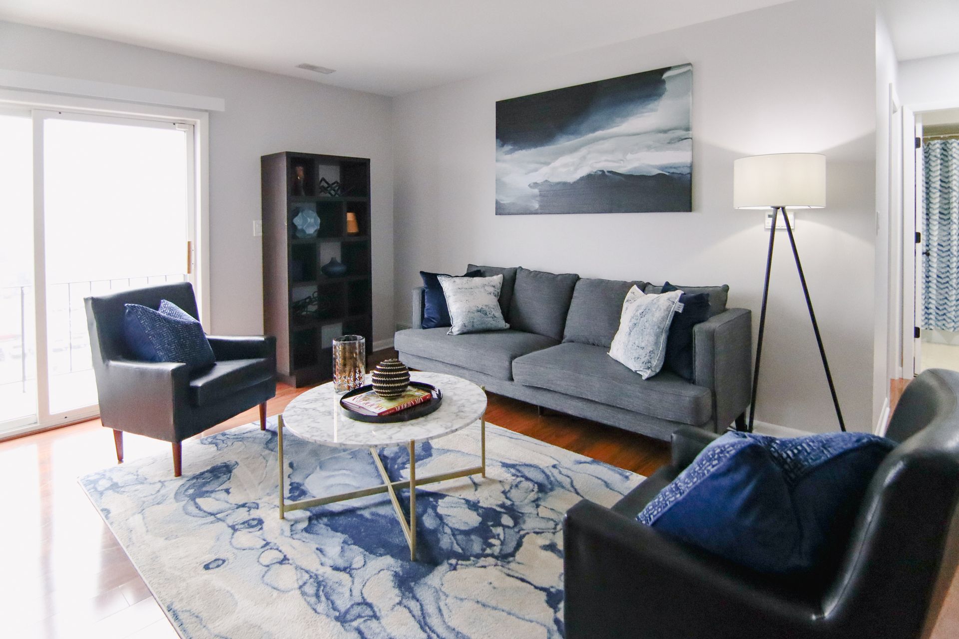 Living room with gray sofa, two black chairs, marble coffee table, and blue and white rug.