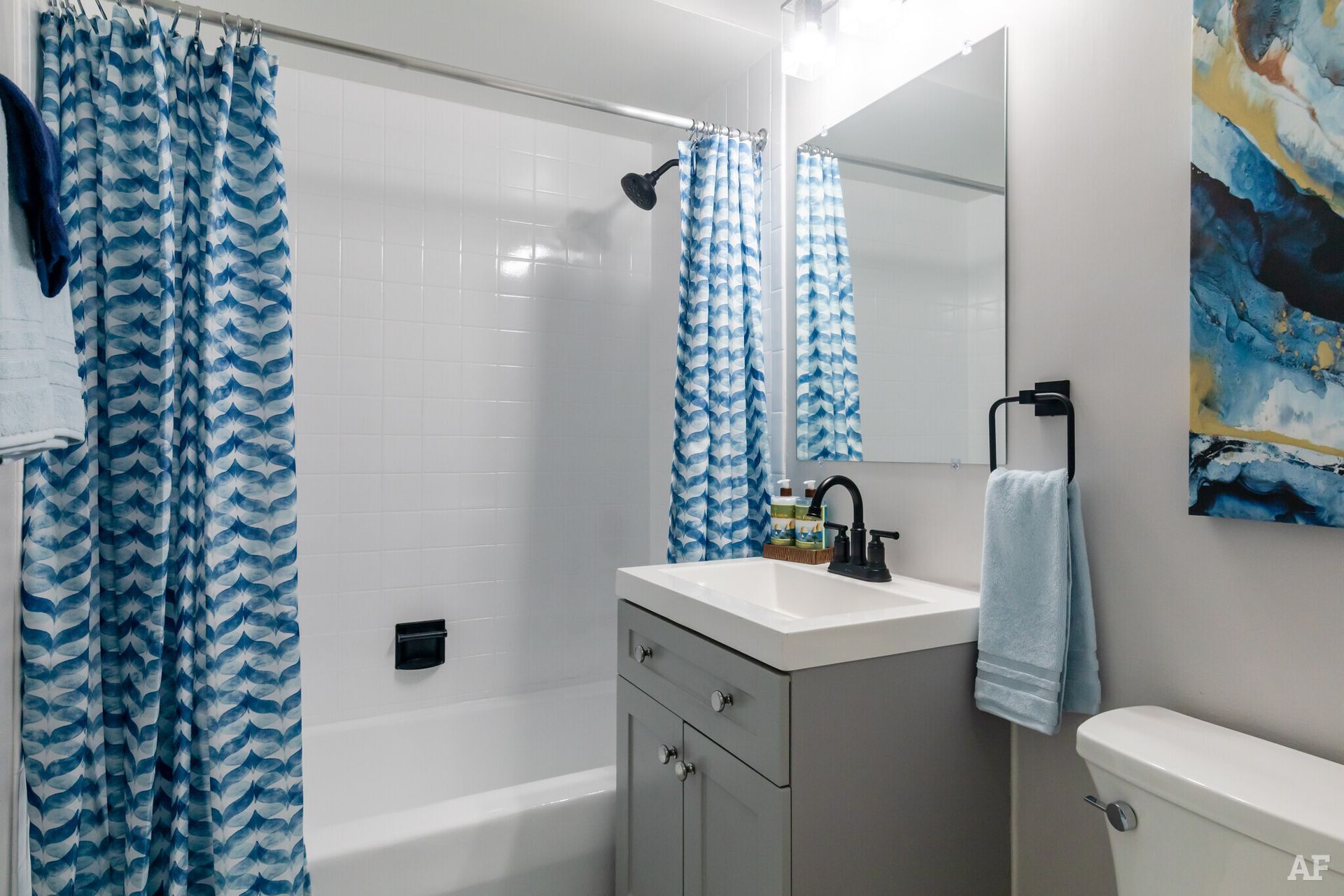 Bathroom with blue and white patterned shower curtain, gray vanity, and a white toilet.