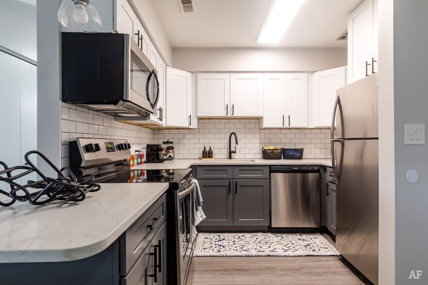 Modern kitchen with gray and white cabinets, stainless steel appliances, and white tile backsplash.