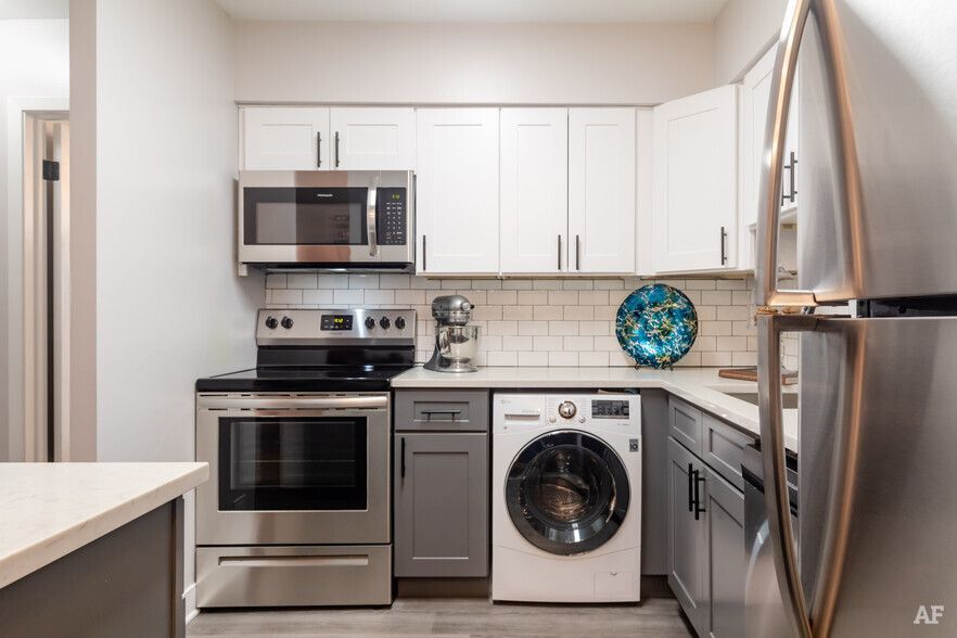 Small kitchen with white and gray cabinets, stainless steel appliances, and a washing machine.