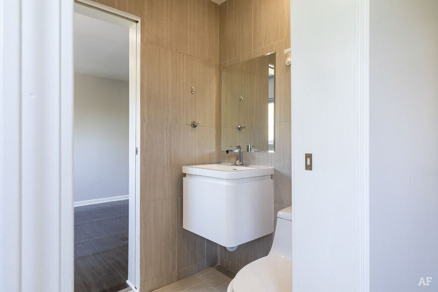 Bathroom with white floating vanity, toilet, and neutral tile. Doorway to room on left.