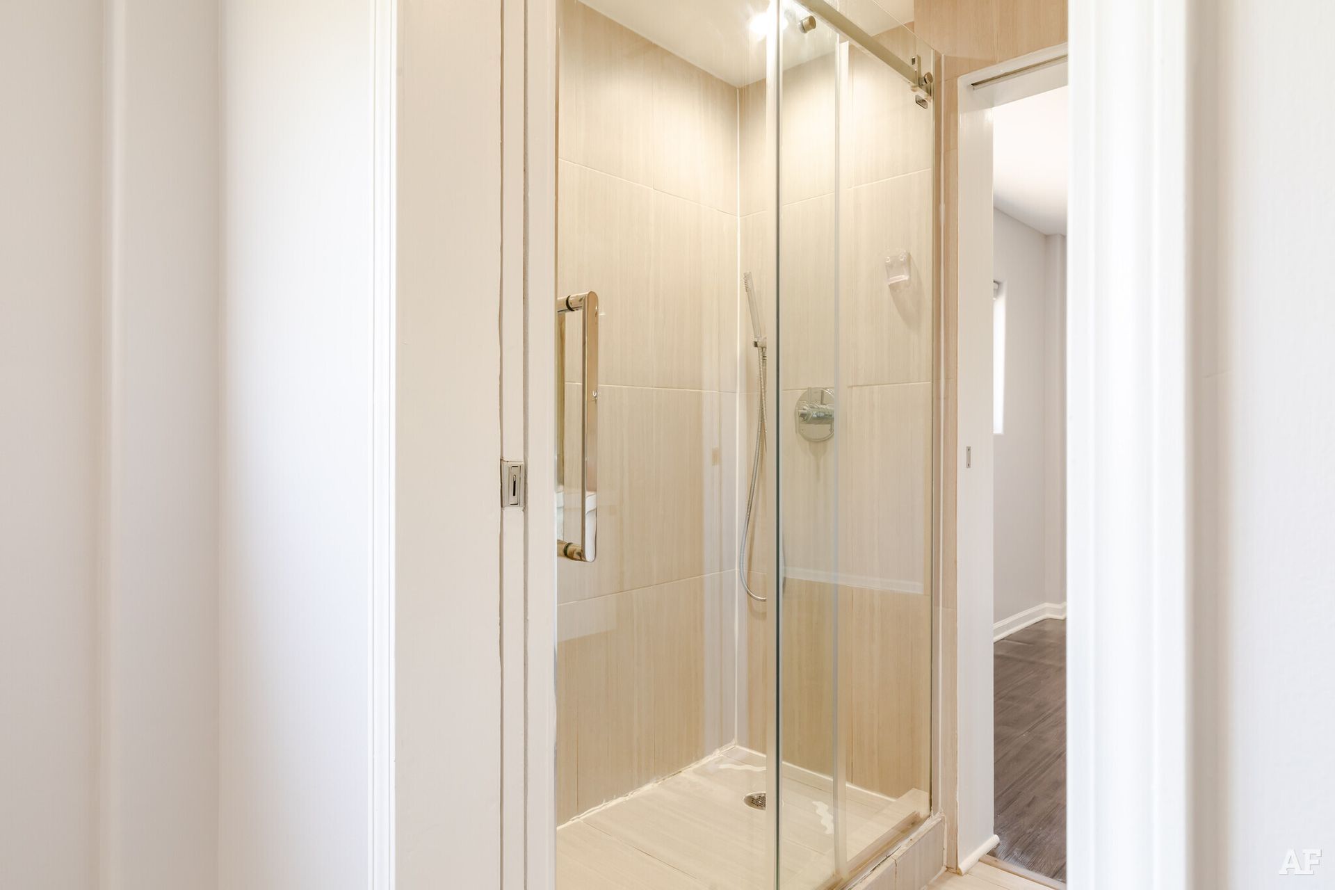 A walk-in shower with glass doors in a bright, white hallway.