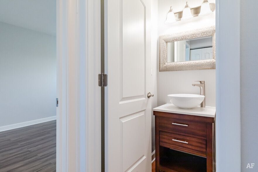 Bathroom interior with a white door, wood vanity, round sink, and decorative mirror.