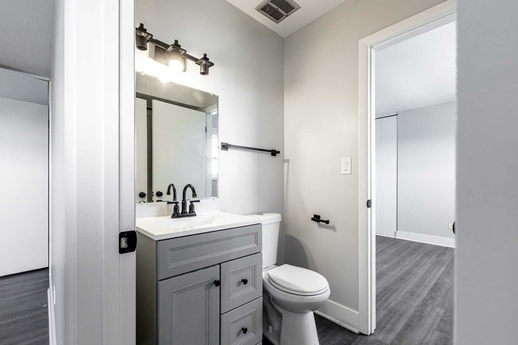 Small gray bathroom with vanity, toilet, and doorway to a room with gray floors.