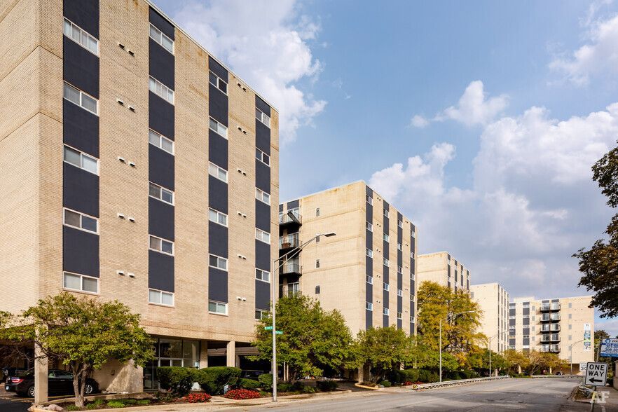 Apartment buildings on a street with trees under a partly cloudy sky.