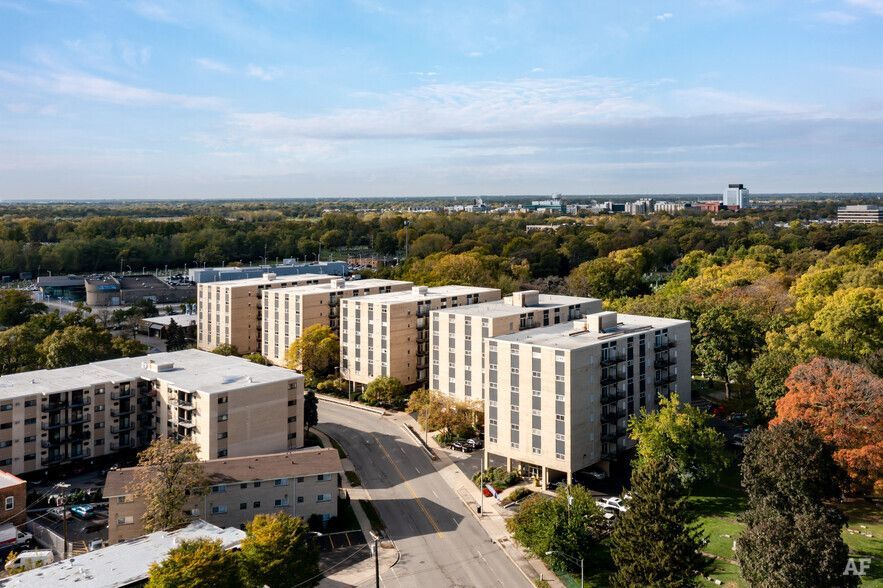 Aerial view of apartment buildings on a street, surrounded by trees, under a blue sky.