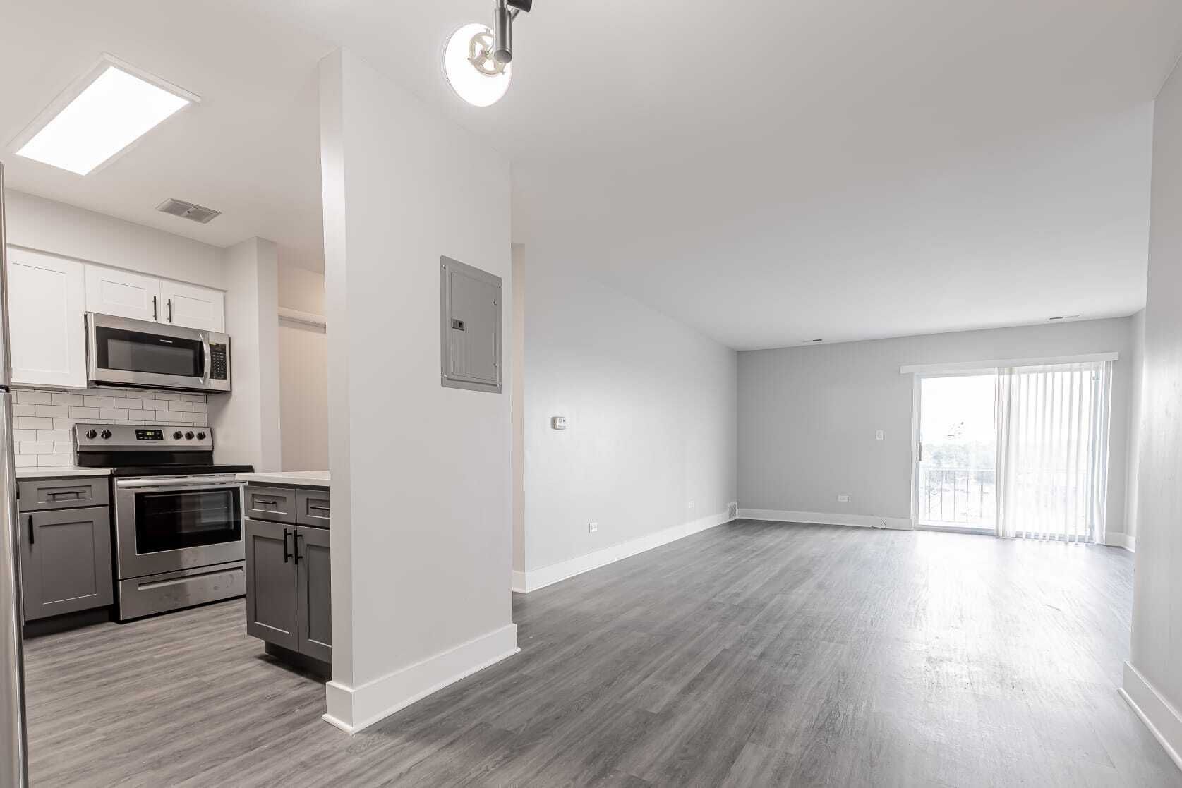 Modern open-concept apartment with gray cabinets, light walls, and a sliding glass door.