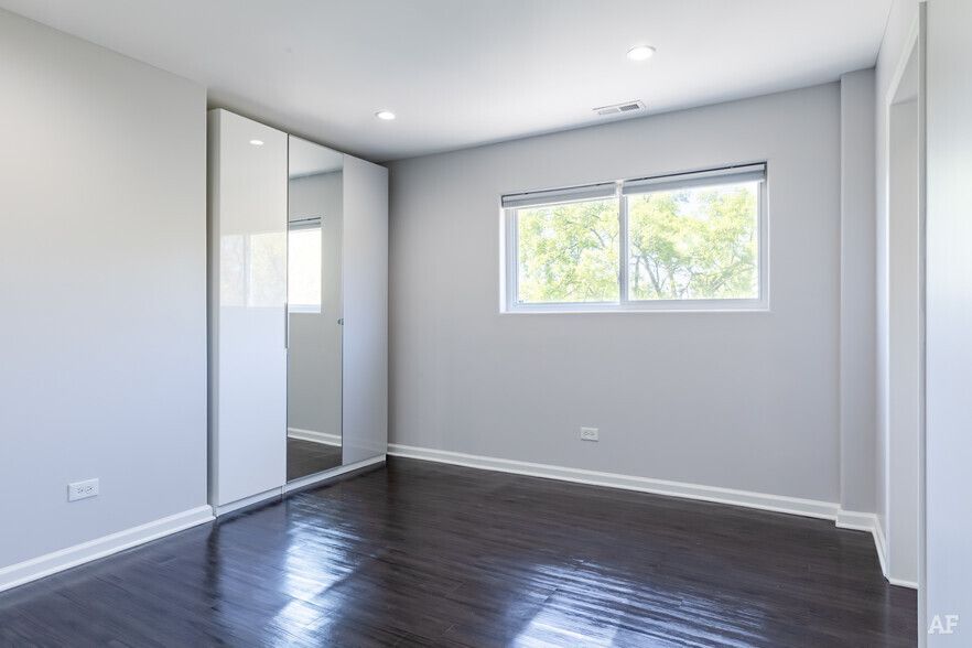 Empty bedroom with gray walls, dark wood floor, large mirrored closet, and window.