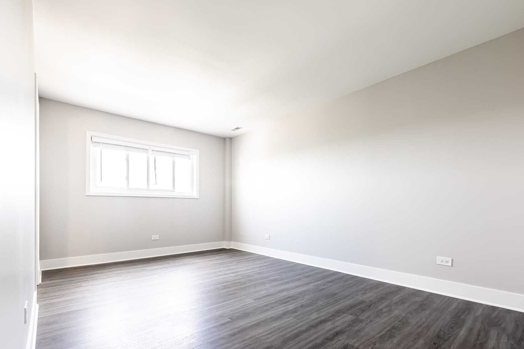 Empty room with gray walls, wood-look floor, and a window with white trim.