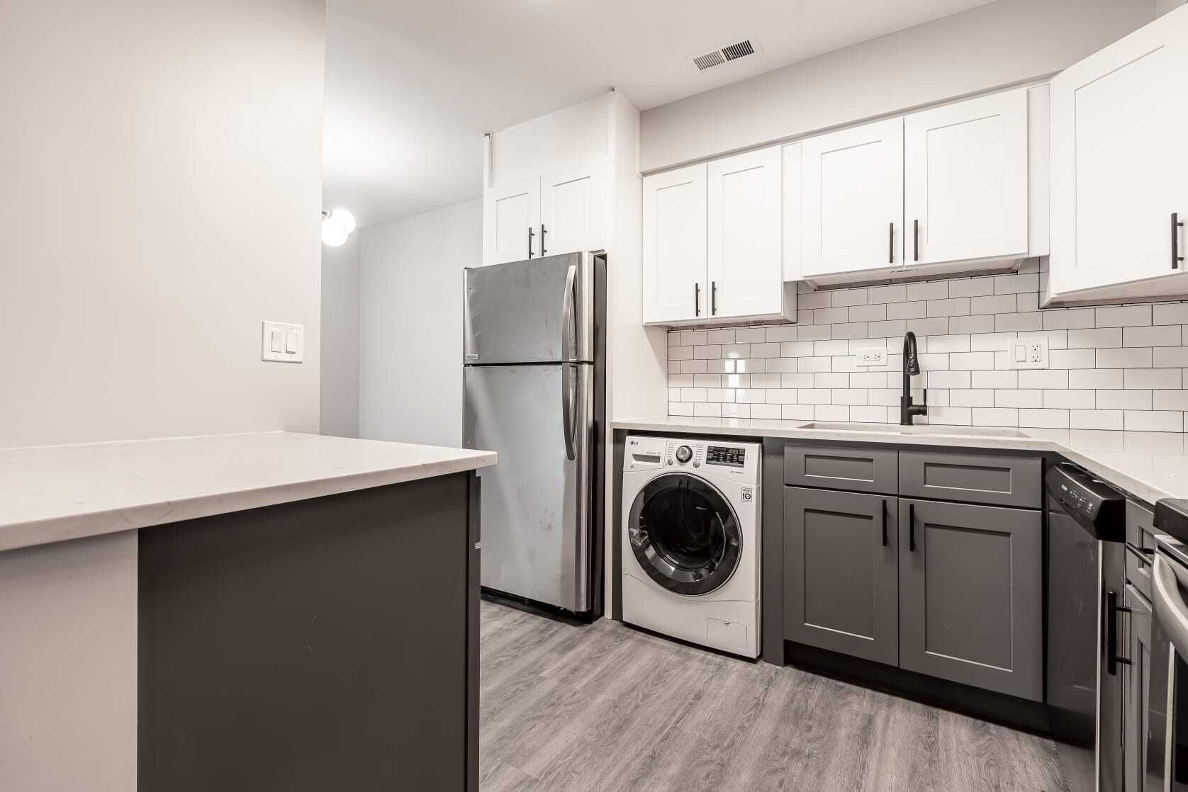 Modern kitchen with white and gray cabinets, stainless steel appliances, and a washer/dryer.