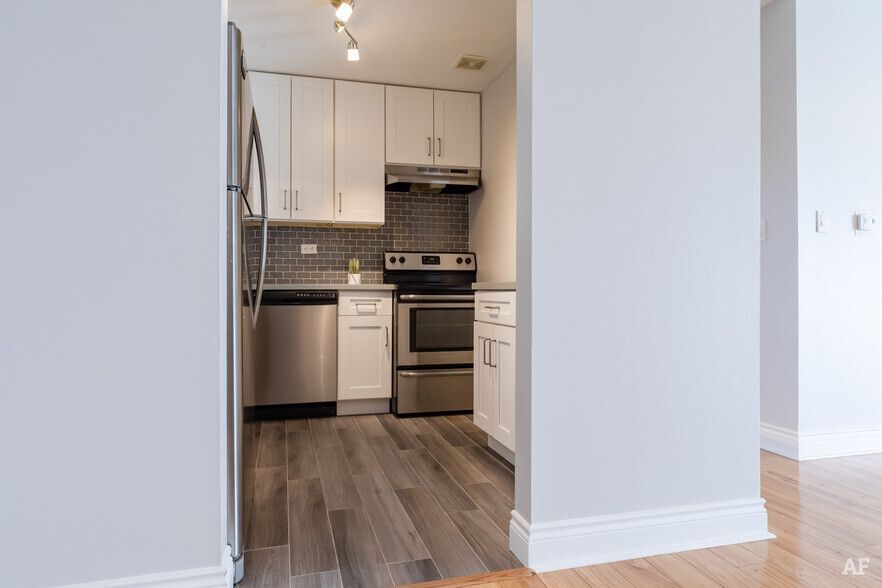 Modern kitchen with stainless steel appliances, white cabinets, and gray tiled backsplash.