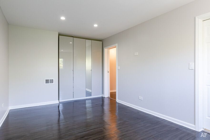 Empty bedroom with gray walls, dark wood floor, and mirrored closet doors.