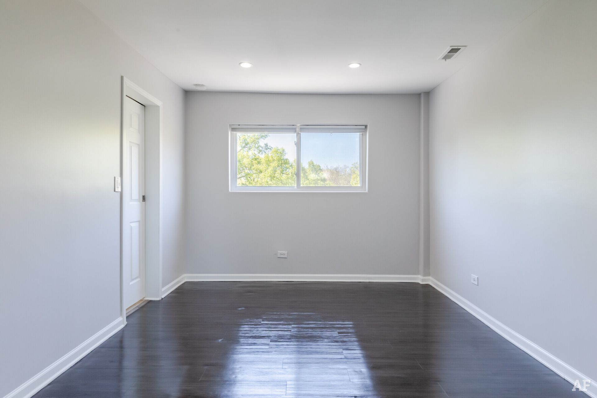 Empty room with dark hardwood floors, light gray walls, and a window.