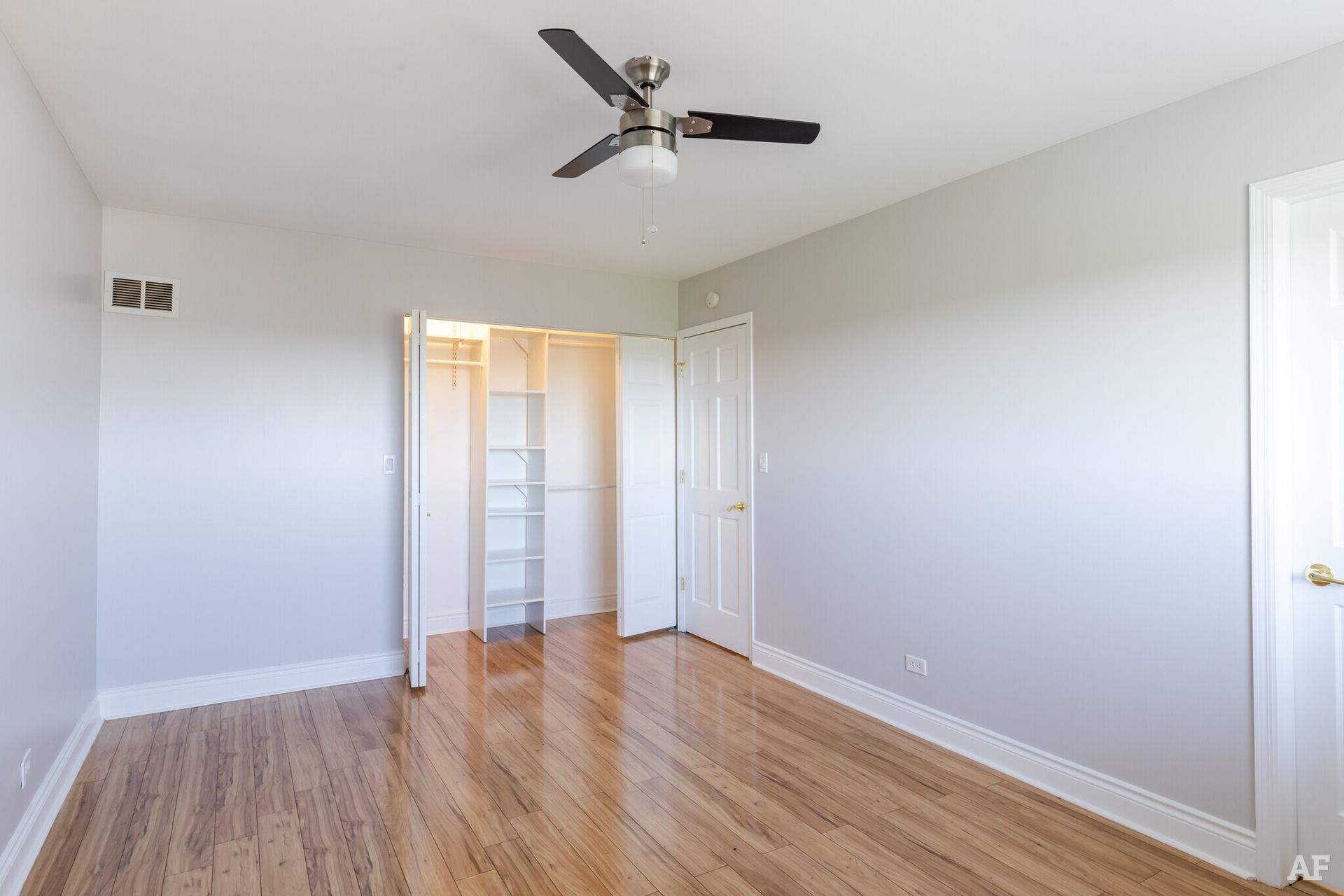 Empty bedroom with hardwood floors, white bi-fold closet doors, and a ceiling fan.