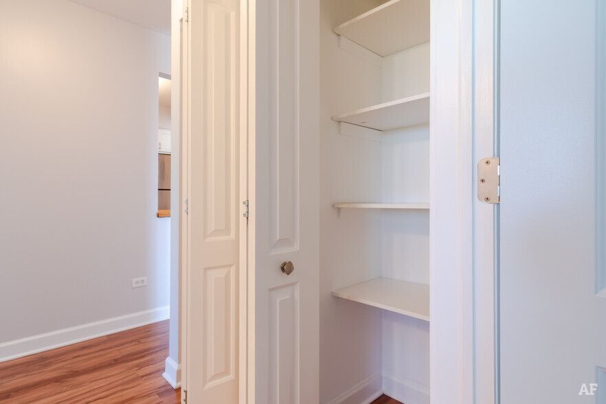 White interior closet with shelves, open next to a hallway with wood floors.