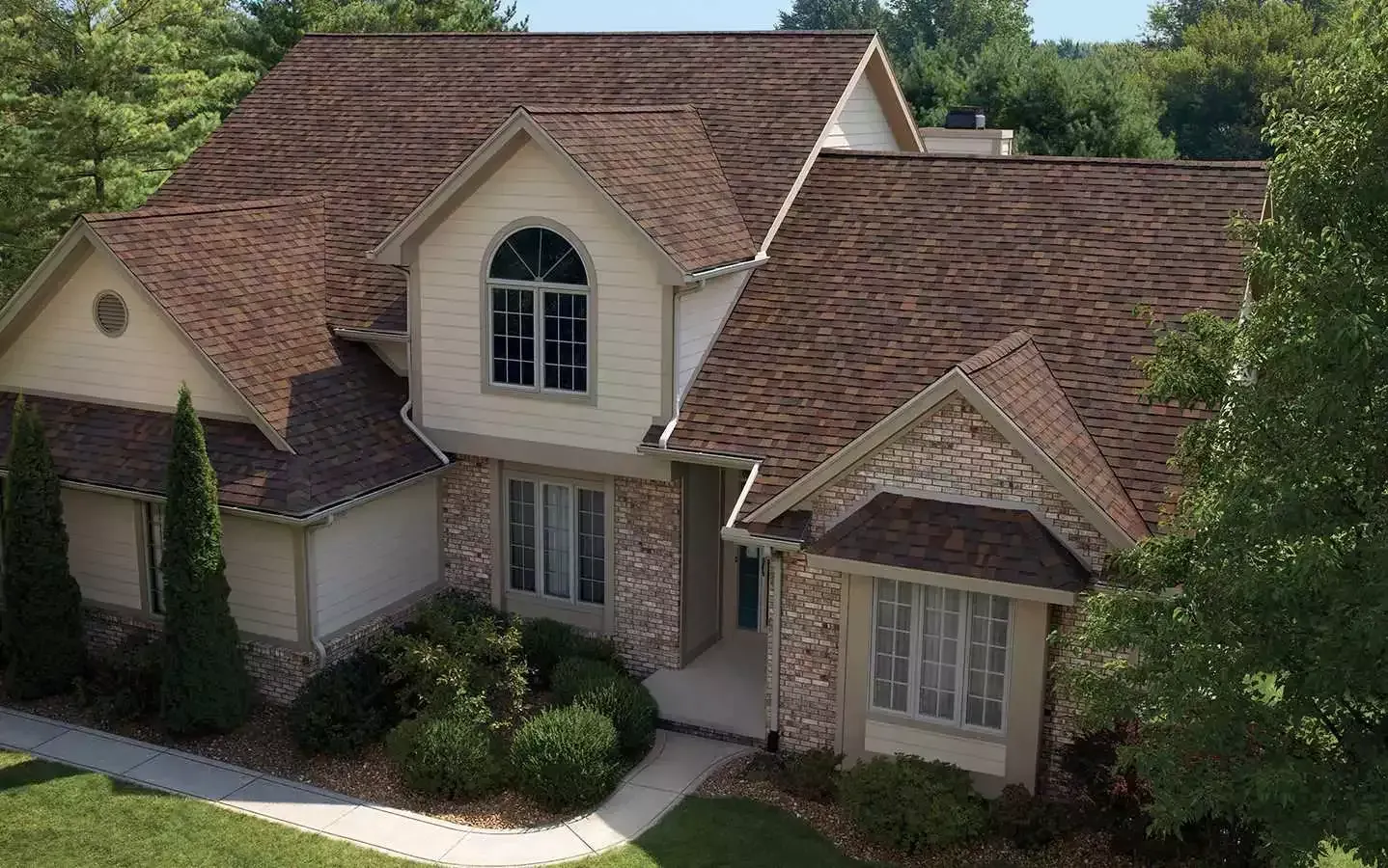An aerial view of a large house with a brown roof surrounded by trees.