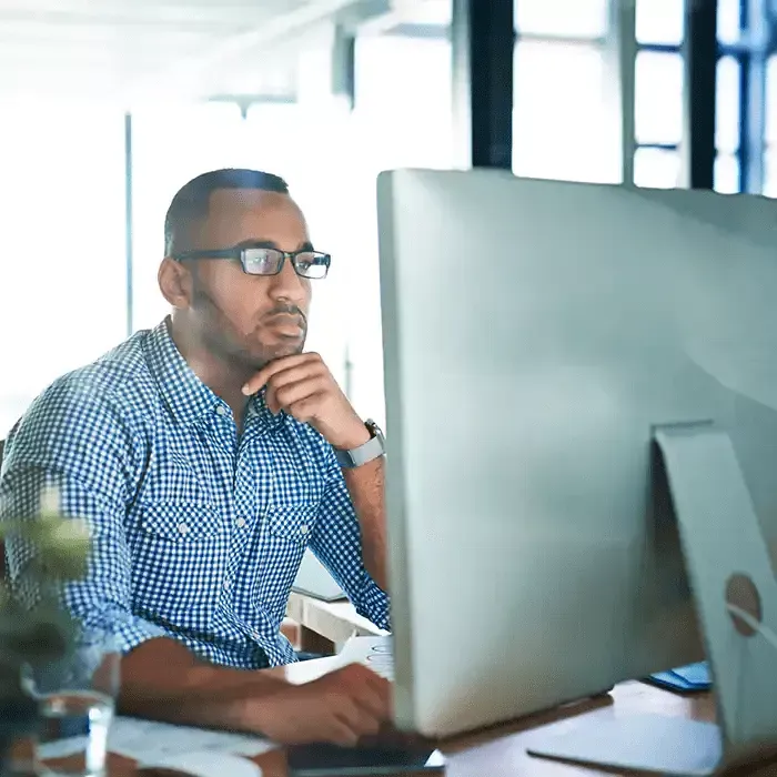 A man wearing glasses is sitting in front of a computer monitor.