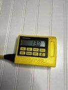 A yellow digital thermometer is sitting on a white table.