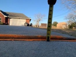 A tape measure is being used to measure the depth of a driveway.