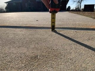 A person is measuring a concrete driveway with a tape measure.