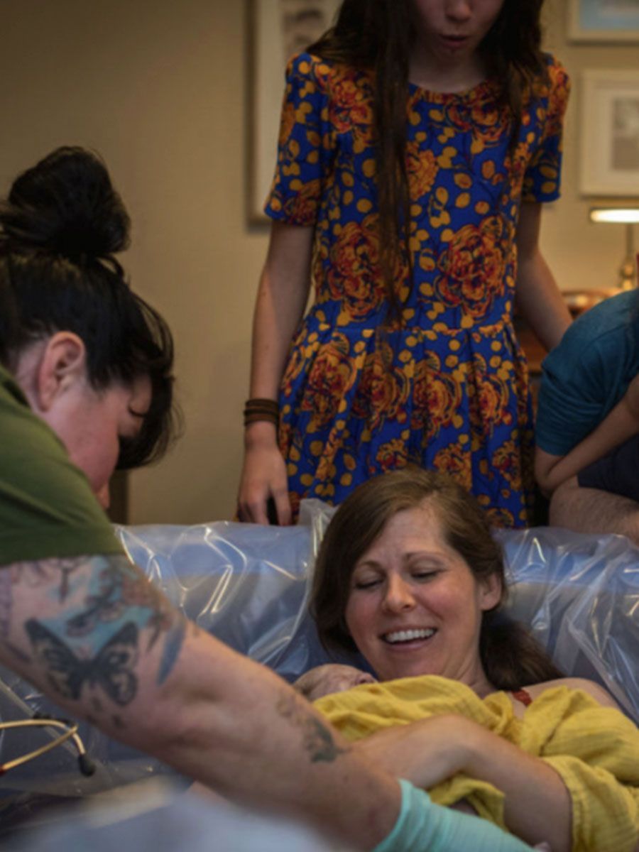 A woman is laying in a tub with a baby while a woman stands behind her.