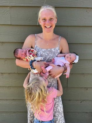 A woman is holding two babies and two little girls.