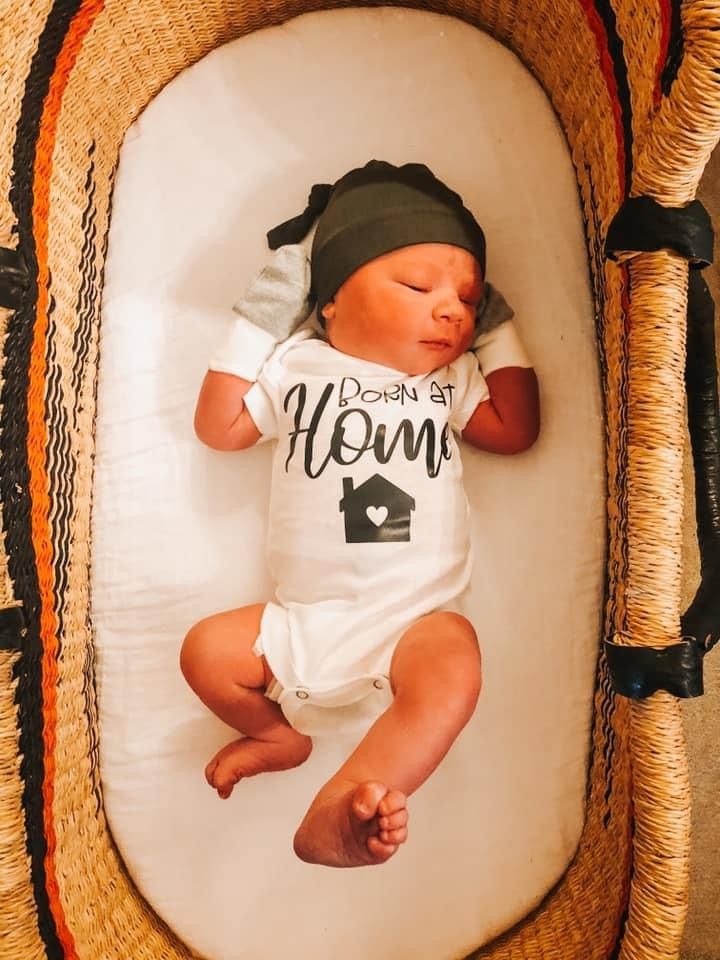 A newborn baby is laying in a basket wearing a shirt that says home