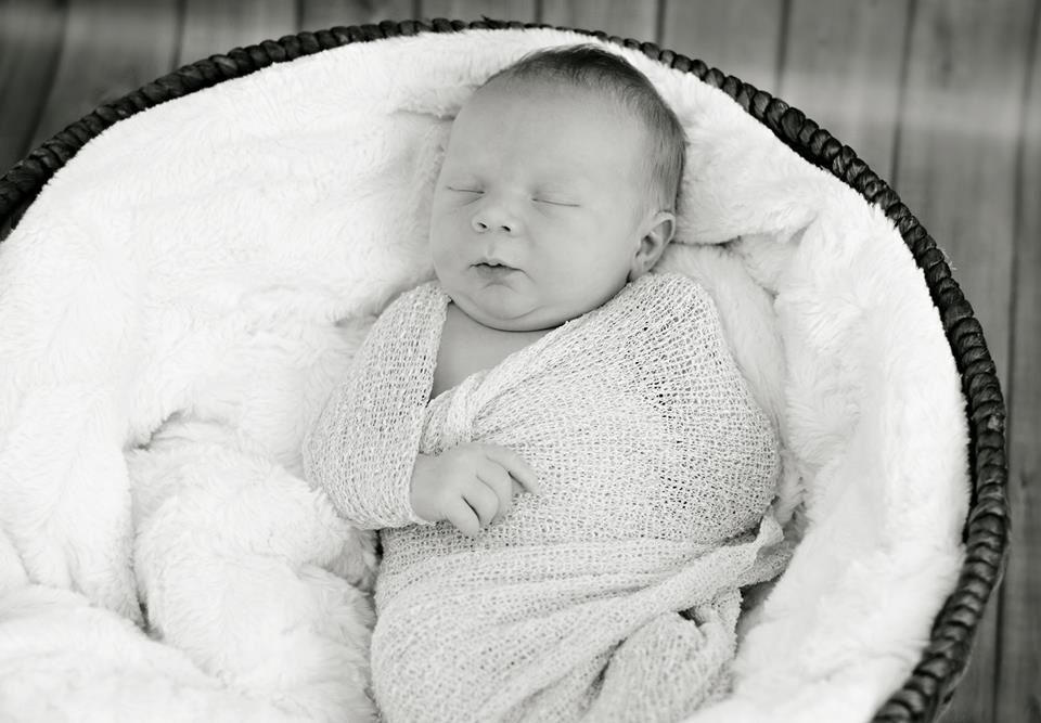 A baby wrapped in a blanket is sleeping in a basket.